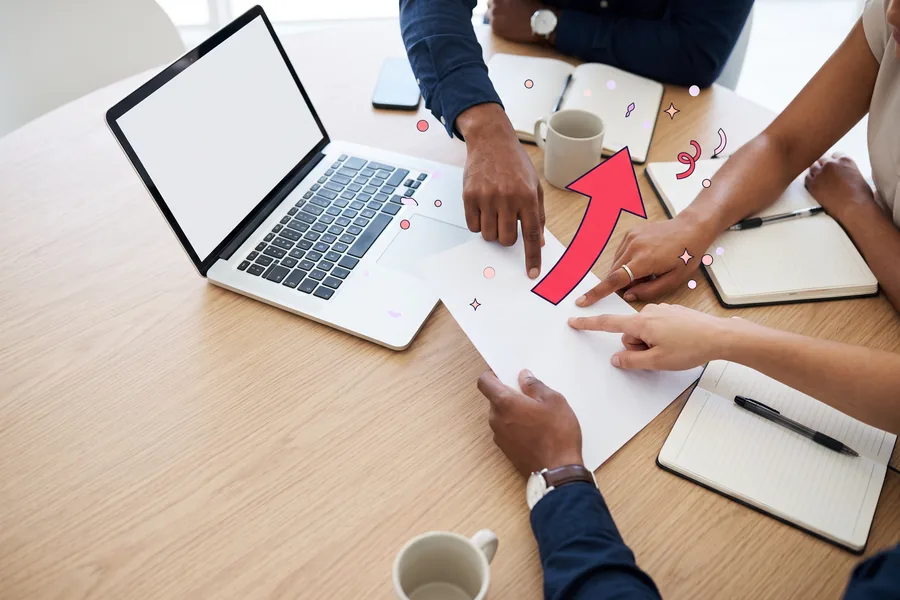 Three colleagues at a meeting table pointing at a printed report beside a laptop