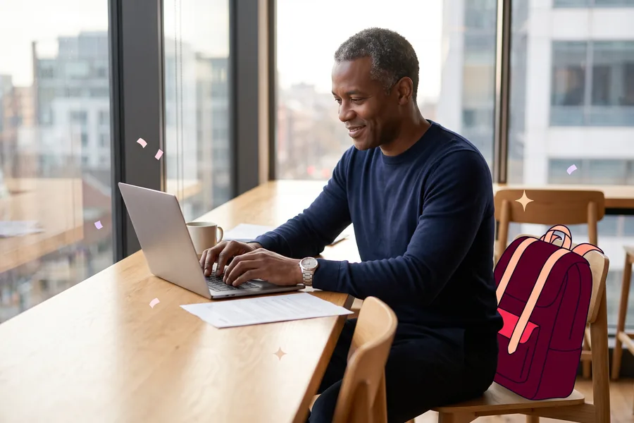 Man typing on a laptop, a leather backpack on the chair beside him