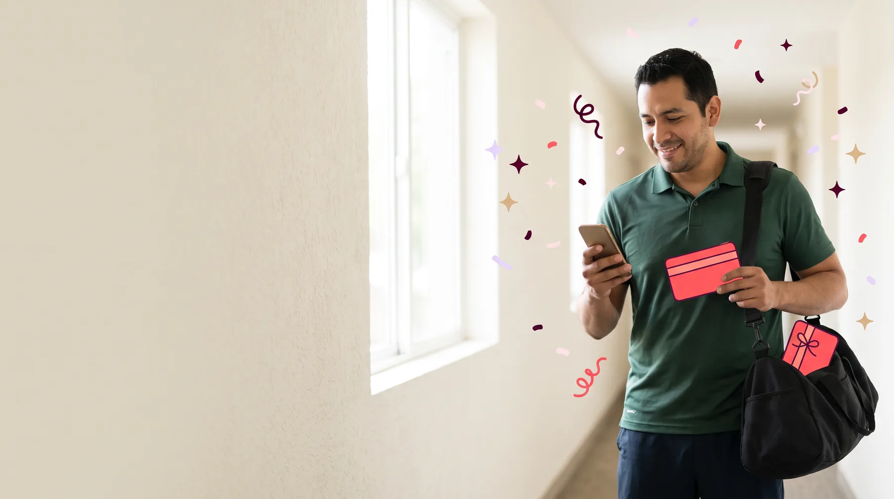 Man in a hallway at home with a gym bag, smiling at his phone and holding a gift card