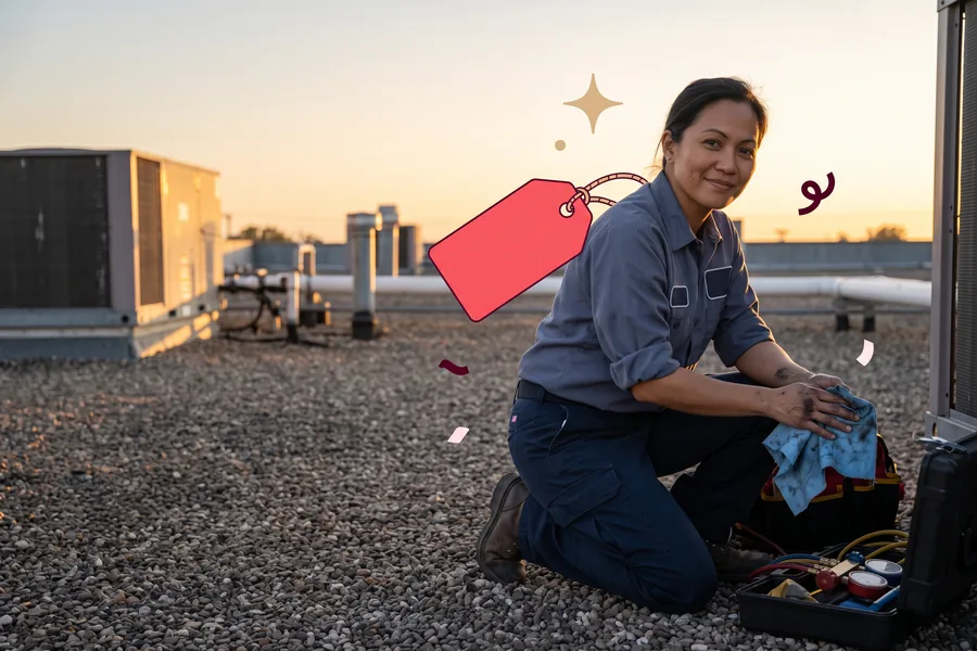 HVAC technician kneeling beside a rooftop unit, wiping her hands on a rag