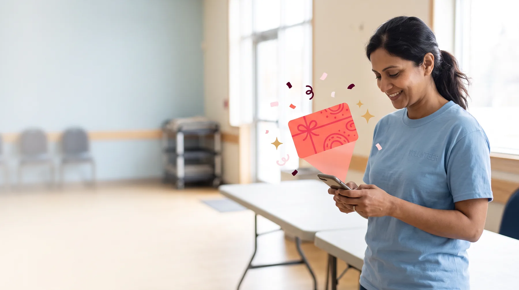 Volunteer beside folding tables at a community center, smiling at her phone