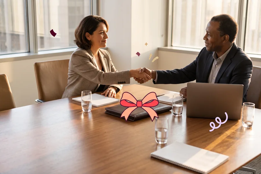 Two people shaking hands across a conference table after signing a deal