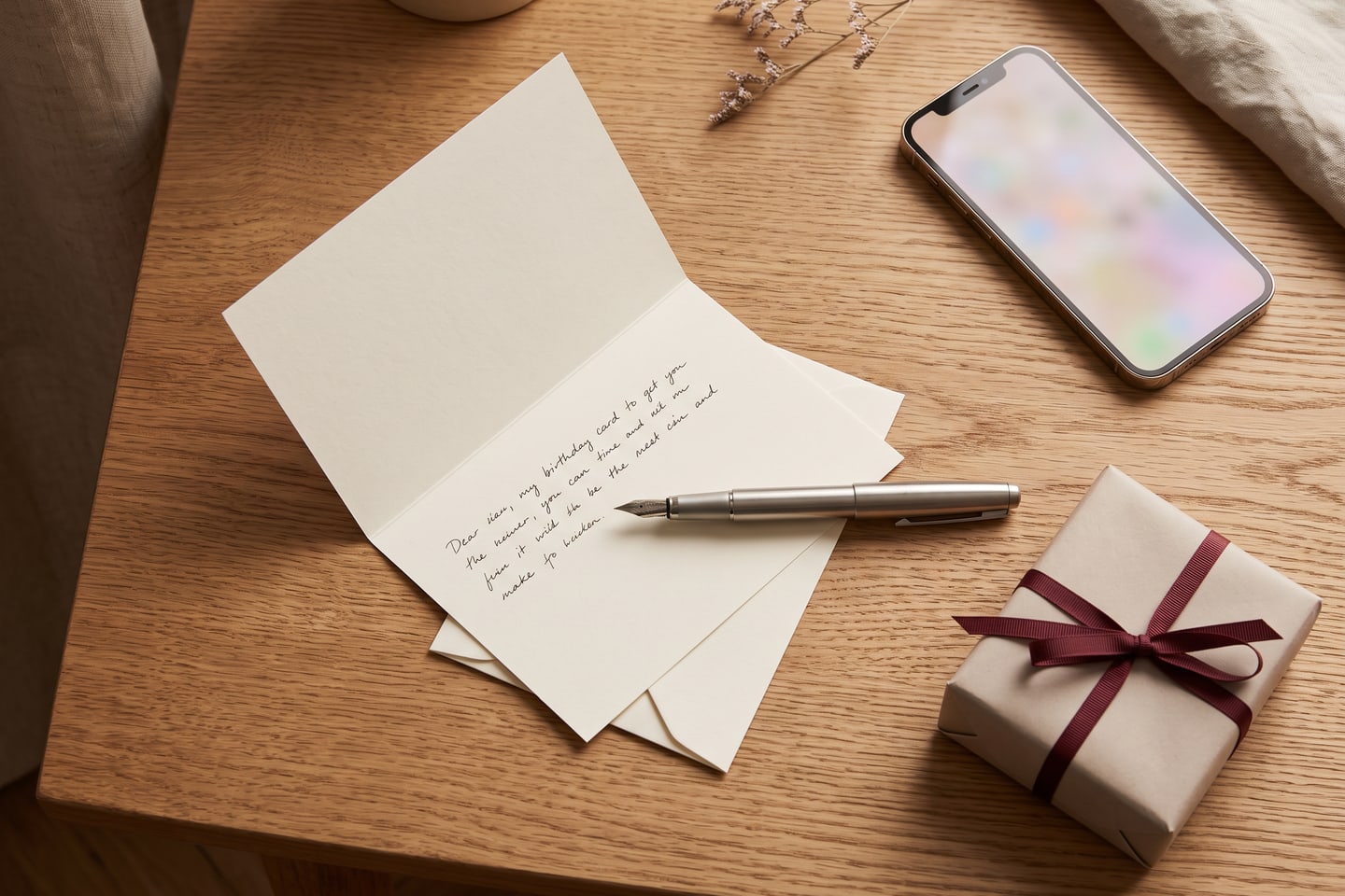 A birthday card being written beside a small wrapped gift and a phone on an oak desk
