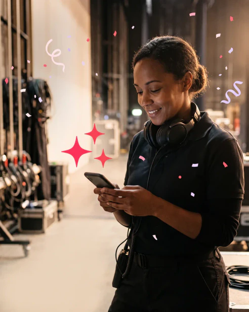 Stage crew member backstage with a headset around her neck, smiling at her phone