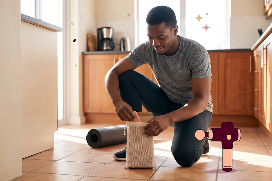 Man on his kitchen floor unpacking a resistance band, a massage gun beside him
