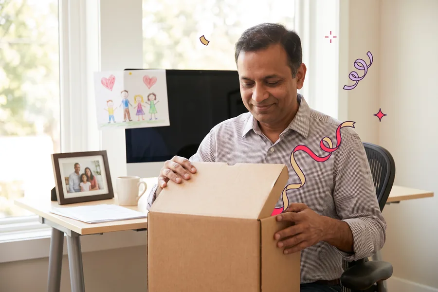 Man opening a gift box at his office desk beside his child's crayon drawing