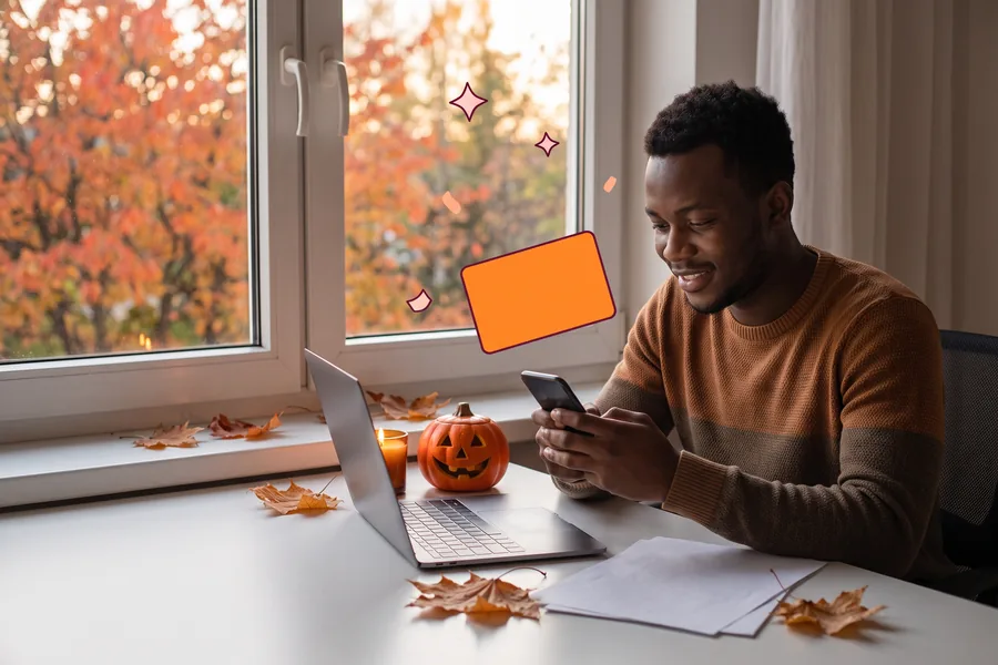 Man at a desk with a small pumpkin and a candle, smiling at a gift link on his phone