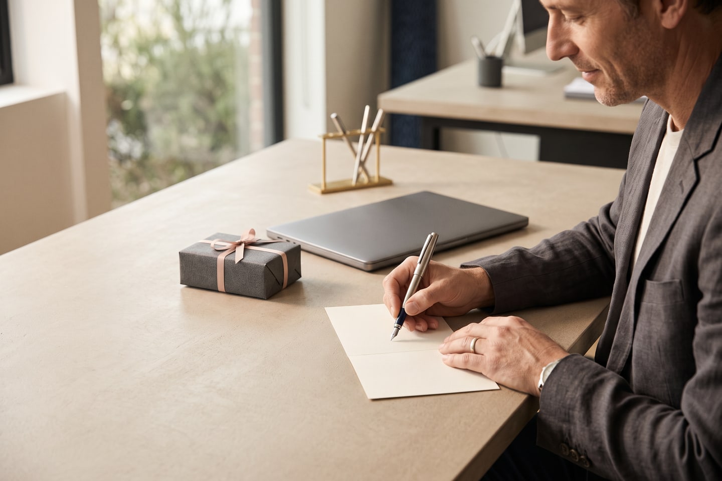 A manager writing a note card at a clean desk beside a small wrapped gift