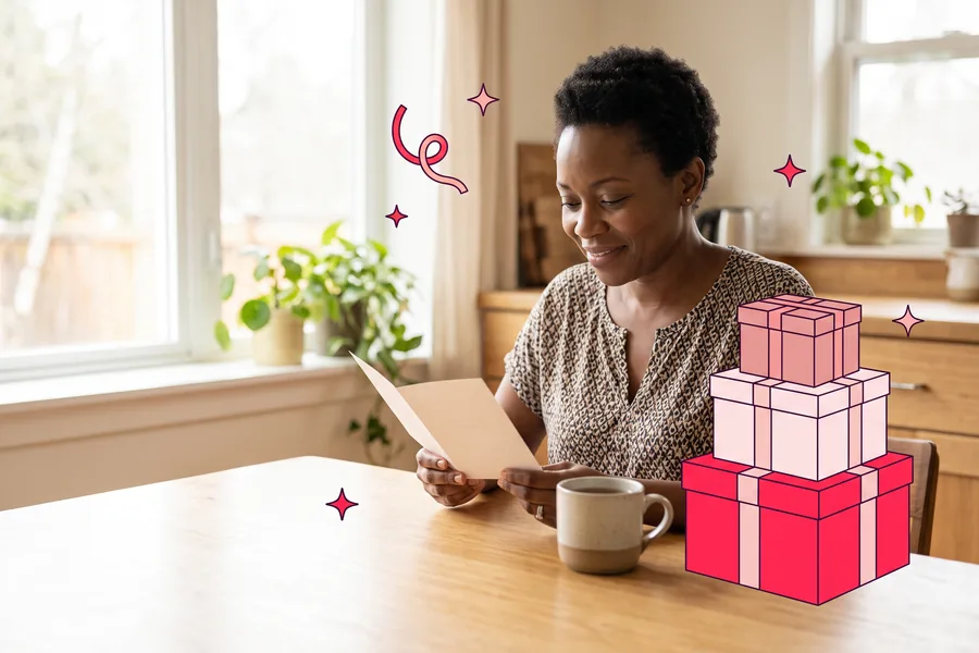 A Nigerian American woman in her mid-forties sits at a kitchen table by a morning window, reading a folded card with a quiet smile beside a mug of tea
