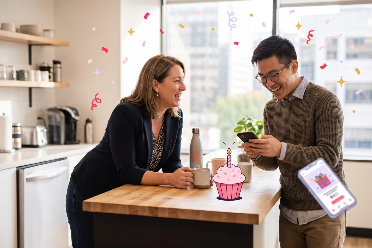 A manager and an employee laughing together at an office kitchen counter while the employee chooses a gift on her phone